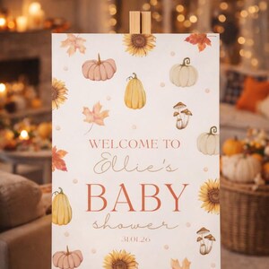 May include: A baby shower sign on an easel, featuring watercolor illustrations of pumpkins, sunflowers, and fall leaves. The sign reads "Welcome to Ellie's BABY shower 31.01.26" in a warm, autumnal color palette.