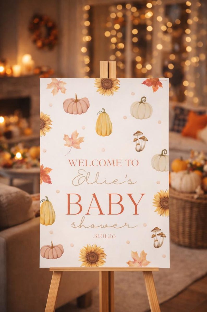 May include: A baby shower sign on an easel, featuring watercolor illustrations of pumpkins, sunflowers, and fall leaves. The sign reads "Welcome to Ellie's BABY shower 31.01.26" in a warm, autumnal color palette.
