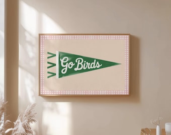 May include: A framed wall art print featuring a green pennant with the words "Go Birds" in white script. The pennant is set against a beige background with a pink and white gingham border, all within a wooden frame.