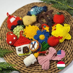 Puede incluir: Una colección de juguetes de ganchillo coloridos, que incluyen un coche rojo, un sol amarillo, una flor azul, una manzana roja y una estrella amarilla. Los juguetes están dispuestos sobre una estera circular tejida, con follaje verde en el fondo.