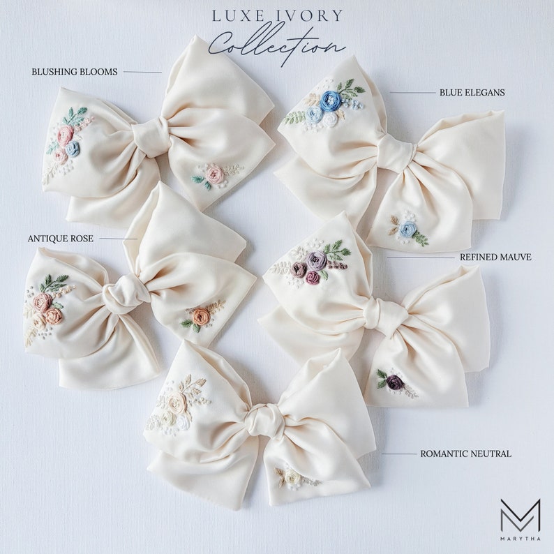 May include: Six ivory satin hair bows with different floral embroidery designs. The designs include antique rose, blushing blooms, blue elegans, refined mauve, and romantic neutral.