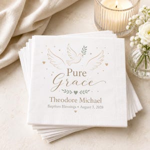 Puede incluir: Una pila de servilletas de papel blanco con un dise&ntilde;o impreso de una paloma con una rama de olivo, corazones peque&ntilde;os y puntos. El texto dice Pure Grace, Theodore Michael, Baptism Blessings y August 3, 2028, en fuentes serif y cursiva.