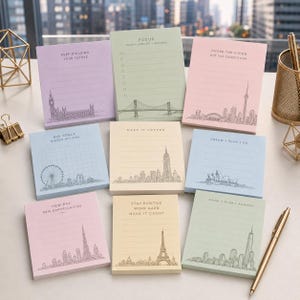May include: A set of pastel-coloured sticky note pads with motivational quotes and city skyline illustrations. Each pad features a different design, including the London Eye, Eiffel Tower, and the Empire State Building. The pads are lined and ready for notes.
