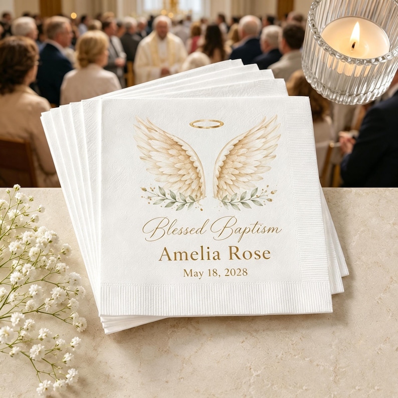 Op de afbeelding: Een stapel witte papieren servetten met een illustratie van een gouden halo en beige engelenvleugels boven groene bladeren. De tekst Blessed Baptism, Amelia Rose en May 18, 2028 staat in een gouden lettertype op het voorste servet.