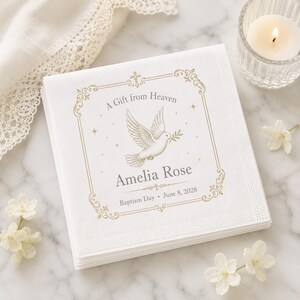 Puede incluir: Una servilleta de papel cuadrada blanca con un borde decorativo dorado, una ilustraci&oacute;n central de una paloma con una rama de olivo y el texto A Gift from Heaven, Amelia Rose y Baptism Day June 8, 2028 impreso en tinta gris y dorada.