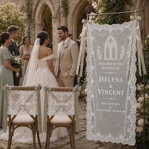 May include: A vertical white lace wedding sign featuring the text Welcome to the wedding of Helena & Vincent, May 24th, 2031, Sacred Heart Church, MA, with a gothic arch graphic, hanging from a metal stand with sage green ribbon bows.