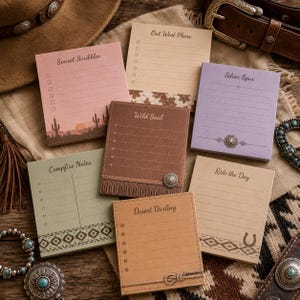 May include: A selection of square notepads with Western-themed designs. The pads feature various colours, including pink, tan, and green, with text such as "Sunset Scribbles" and "Wild Soul." Decorative elements include cacti, fringe, and a horseshoe.