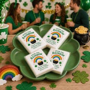 May include: Four stacks of white paper napkins in clear plastic packaging, each printed with a colourful rainbow, a black pot of gold, and the text Over the Rainbow, Good Times & Green Vibes, Ethan's Party, arranged on a green clover-shaped tray.