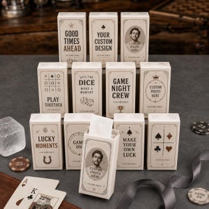 May include: A collection of rectangular white boxes for playing cards, each featuring distinct black text and graphic designs. Some boxes display phrases like Good Times Ahead, Play Together, or Game Night Crew, while others include custom photo frames.