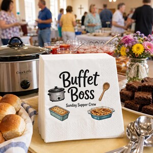 Puede incluir: Una pila de servilletas de papel blancas con el texto negro "Buffet Boss" y "Sunday Supper Crew" con ilustraciones de una olla de cocción lenta, una cuchara de madera, un pan en un molde y un guiso en una fuente azul.