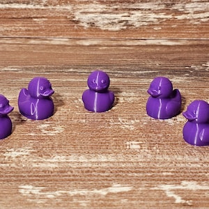 May include: Five purple rubber duck figurines arranged in a row on a wooden surface.