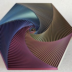 Könnte beinhalten: Ein sechseckiges geometrisches Wandkunstwerk aus Metall mit einem wirbelnden Muster in Blau, Lila und Gold.