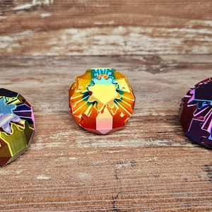 Pode incluir: Três formas geométricas iridescentes e multifacetadas com um esquema de cores arco-íris. As formas estão dispostas em fila sobre uma superfície de madeira.