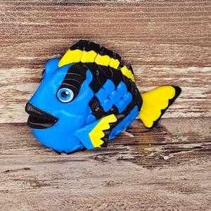 May include: A blue and black fish figurine with yellow fins. The fish has a large eye and a small mouth. The figurine is made of a smooth, hard material and is about 3 inches long.