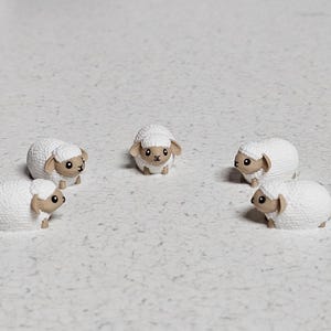 Op de afbeelding: Vijf witte schapenfiguren met bruine gezichten en zwarte ogen zijn in een cirkel op een wit oppervlak gerangschikt.