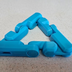 May include: A blue plastic toy made of interlocking pieces that can be arranged into different shapes. The toy is in the shape of a triangle.