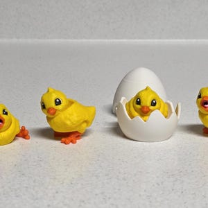 May include: A collection of four yellow chick figurines with orange feet and beaks. One chick is inside a white egg, and the others are positioned around it. These figurines are likely Easter or spring-themed decorations.