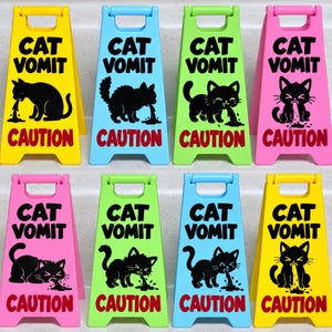May include: Eight miniature A-frame caution signs in yellow, blue, green, and pink plastic. Each sign features the black text CAT VOMIT above a black graphic of a cat vomiting, with the red text CAUTION printed at the bottom of each unit.