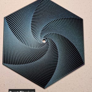 May include: A dark blue, hexagonal, geometric design with a swirling pattern. The design is made of thin lines that create a sense of depth and movement. The text "Burnt Titanium" is visible below the design.