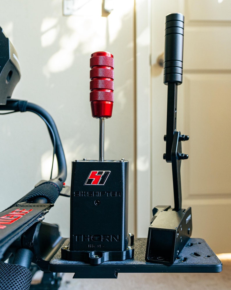 May include: A black shifter with a red knob and the text "SHIFTER" and "THORN" printed on it. The shifter is mounted on a black metal plate.