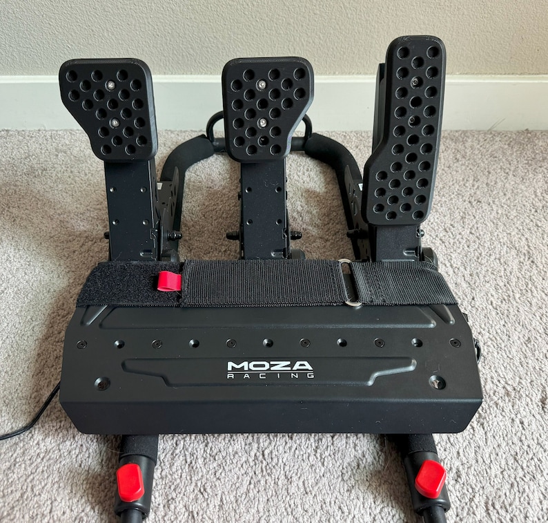 May include: Black racing pedals with a black base and red accents. The pedals are labeled "MOZA RACING".