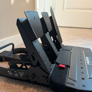 May include: Black racing pedals with a metal frame and adjustable pedals. The pedals are labeled "MOZA RACING".