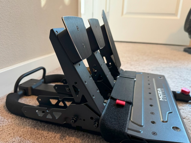 May include: Black racing pedals with a metal frame and adjustable pedals. The pedals are labeled "MOZA RACING".