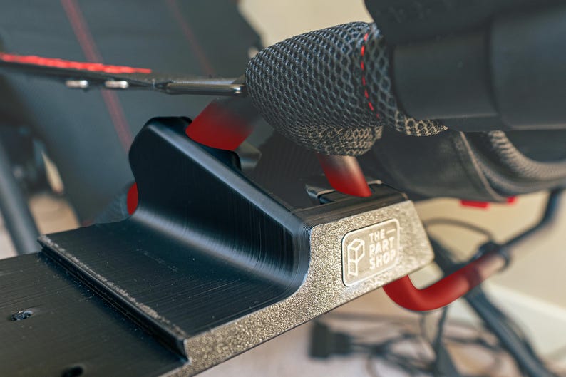 May include: Close-up of a black metal bracket with a red strap attached. The bracket has a textured surface and a logo that reads "The Part Shop".