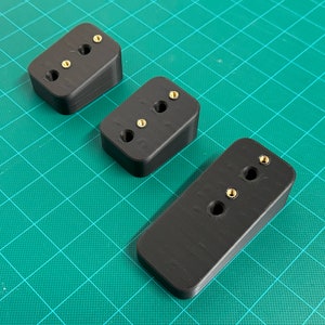 May include: Three black plastic blocks with three gold screws each. The blocks are angled and have a textured surface.