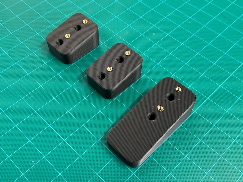 May include: Three black plastic blocks with three gold screws each. The blocks are angled and have a textured surface.