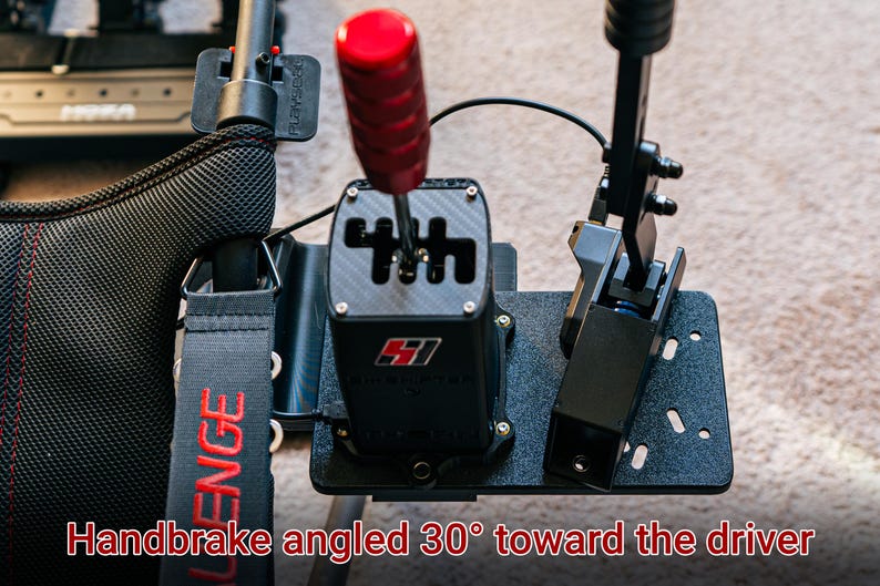 May include: A black racing simulator shifter with a red gear knob and a black handbrake angled 30 degrees towards the driver. The shifter has a carbon fiber look and the text "SH1FT" is printed on the front.