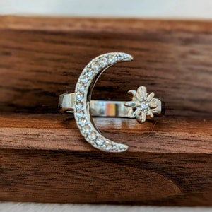 May include: A silver ring with a crescent moon and a star design. The moon and star are both encrusted with small, clear stones.