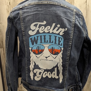 May include: A blue denim jacket with a white graphic on the back. The graphic features a cartoon image of Willie Nelson with the text "Feelin' Willie Good".