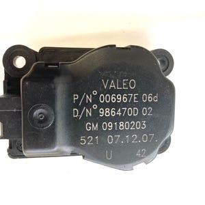 May include: Black plastic automotive part with the text "VALEO P/N° 006967E 06d D/N° 986470D 02 GM 09180203 521 07.12.07. U 42" printed on it.