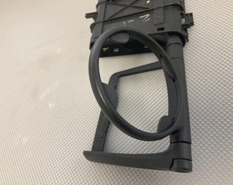 May include: Black plastic cup holder with a circular opening. The holder is designed to fit into a car's dashboard.