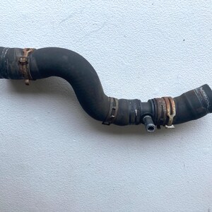 May include: A black, curved automotive rubber coolant hose featuring three integrated metal tension clamps and a small, protruding silver-colored metal pipe connector extending from the side of the main hose body.