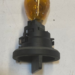 May include: A black and yellow car light bulb with a plastic base. The bulb is amber coloured and has a metal filament inside. The base is black and has a small tab on the side.