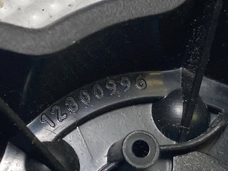 May include: Close-up of a black plastic component with the number "12800996" embossed on its surface. The component has a circular hole and a rounded, protruding feature. The image is well-lit, highlighting the details of the molded plastic.