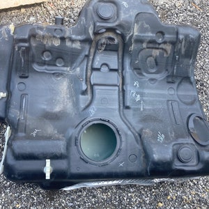 May include: A black plastic fuel tank with a large circular opening and several smaller openings. The tank has handwritten markings on it, including "21/2" and "188".