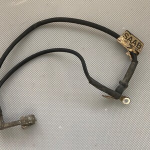 May include: A black wire with two ends, one with a metal connector and the other with a metal ring. The wire has a label that says "SAAB".