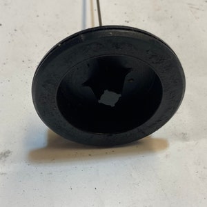 May include: A black plastic cap with a metal rod extending from the center. The cap has a star-shaped opening in the center.