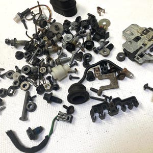 May include: A collection of various metal hardware components, including screws, bolts, nuts, washers, and plastic connectors. The hardware is in various sizes and shapes, with a mix of silver, black, and white colors.