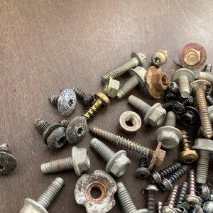 May include: A close-up of a variety of screws and bolts, some with a silver finish and others with a gold finish. The screws and bolts are scattered on a brown wooden surface.