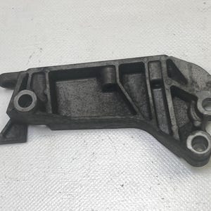 May include: A dark gray metal bracket with multiple holes and a unique shape. The bracket has a textured surface and appears to be a component of a larger mechanical assembly. The design includes a triangular extension and several circular openings.