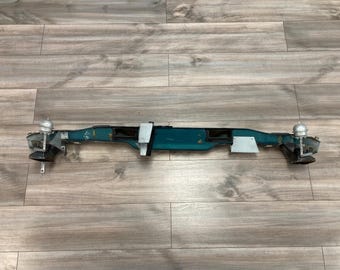 May include: A teal-coloured car part with silver accents. The part has a rectangular shape and is made of metal. It has two small round knobs on either end.