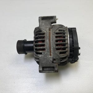 May include: A used automotive alternator with a black pulley and a black threaded end. The alternator has a gray metal housing with visible copper wiring and a black plastic component. The item is likely a replacement part.