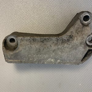 May include: A silver metal engine mount with three holes. The mount is dirty and has a few scratches.