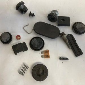 May include: Assortment of black plastic car parts, including a spring, a fuse, a bolt, and various caps and plugs.