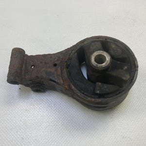 Peut inclure: Une pièce automobile rouillée et usagée, probablement un support moteur. Le composant métallique est brun avec des signes de corrosion. La partie en caoutchouc est noire.