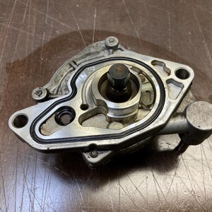 May include: A silver-colored metal automotive oil pump featuring a central rotating shaft, a black rubber gasket seal outlining the internal channels, and multiple mounting holes. The component has a machined finish with visible metallic textures.